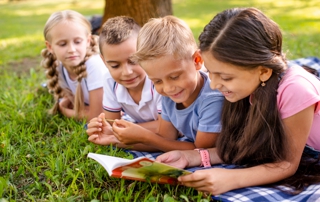 quatre enfants lisent un livre sur l'herbe